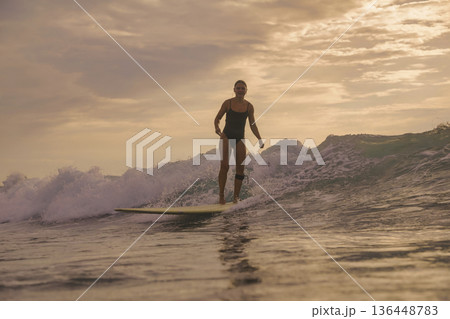 Graceful Female Surfer Maintains Poised Stance During Sunset Surf 136448783