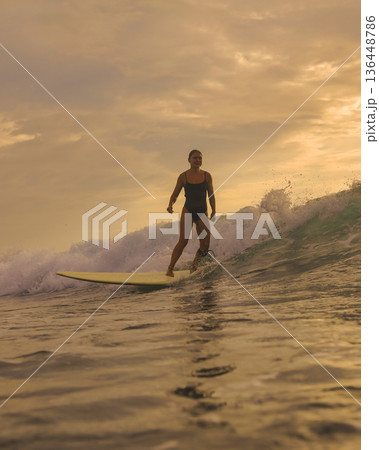 Graceful Female Surfer Enjoying Tranquil Sunset On Her Longboard 136448786
