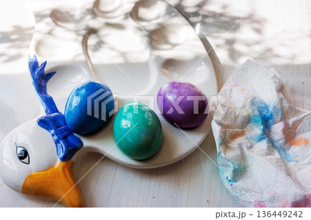 Top view of blue, green, and purple dyed easter eggs placed in molded egg holders on a decorative easter duck serving plate, 136449242