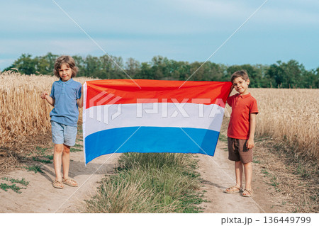 Children Standing With Flag Of Netherlands On Open Wheat Road Field.Happy Future Children Standing With Flag Of Netherlands On Open Wheat Road Field.Happy Future 136449799