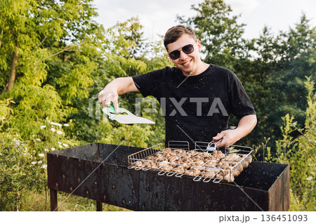Man seasoning mushrooms on barbecue grill outdoors, summer picnic cooking 136451093