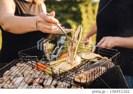 Closeup of vegetables and mushrooms grilling on barbecue with hands turning food outdoors Closeup of vegetables and mushrooms grilling on barbecue with hands turning food outdoors 136451102