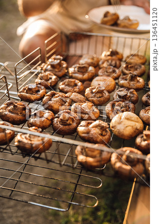 Grilled mushrooms in BBQ basket at outdoor picnic, hands turning food 136451120