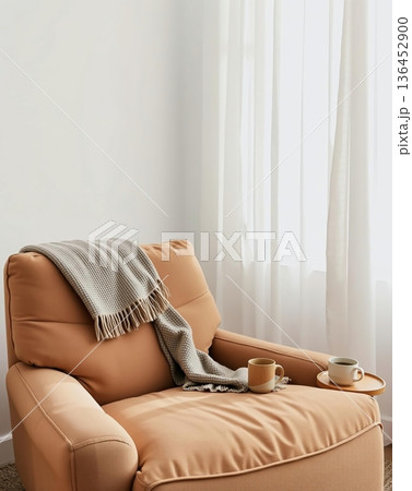 Cozy armchair with a blanket, coffee mugs, and soft curtains, creating a relaxing atmosphere. 136452900
