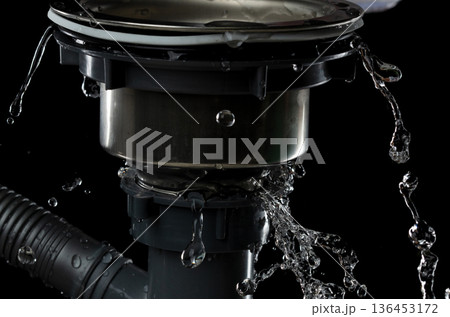 Drain sink leak water from pipe plumbing in bathroom as water splash clogged drop. Pouring Leaking water from gray plastic pipe drain sink. Black background isolated 136453172