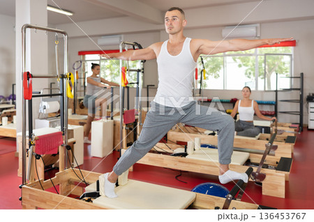 Sportive young guy training her arms and legs on reformer device Sportive young guy training her arms and legs on reformer device 136453767