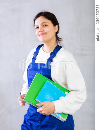 Positive female builder in blue jumpsuit holding engineering documentation 136453785