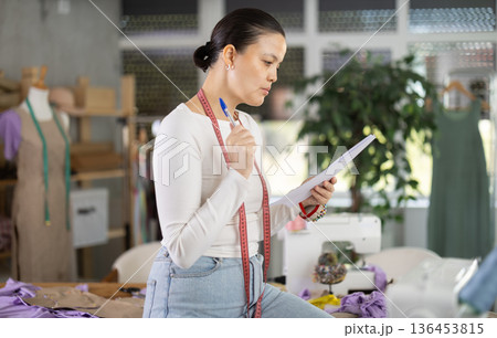 Puzzled dressmaker with documents in her hands 136453815