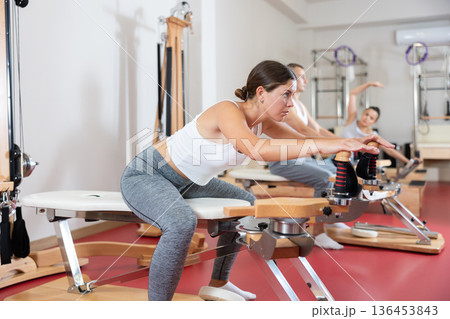 Sportive young girl training her arms turning handle of exercise machine Sportive young girl training her arms turning handle of exercise machine 136453843