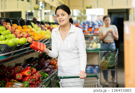 Positive woman picking bell peppers at grocery supermarket Positive woman picking bell peppers at grocery supermarket 136453865