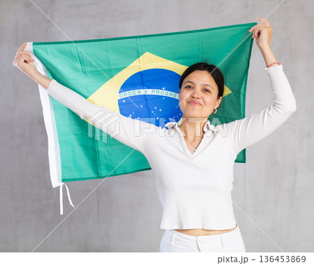 Pretty smiling female football fan holding Brazilian flag 136453869