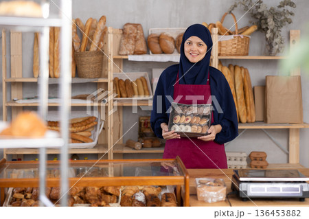 Middle-aged Muslim saleswoman holds cookie box in bakery Middle-aged Muslim saleswoman holds cookie box in bakery 136453882