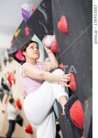Sporty woman climbing on bouldering wall demonstrating physical strength, technical skill, and determination Sporty woman climbing on bouldering wall demonstrating physical strength, technical skill, and determination 136453887