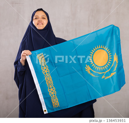 Young Muslim woman in blue hijab holds unfurled flag of Kazakhstan Young Muslim woman in blue hijab holds unfurled flag of Kazakhstan 136453931
