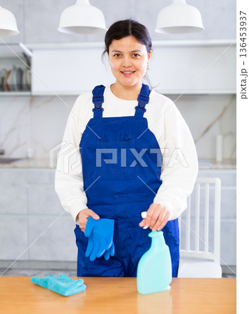 Young smiling cleaning lady standing in home kitchen with detergent 136453937