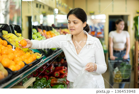 Young asian woman chooses quality juicy ripe tangerines Young asian woman chooses quality juicy ripe tangerines 136453948