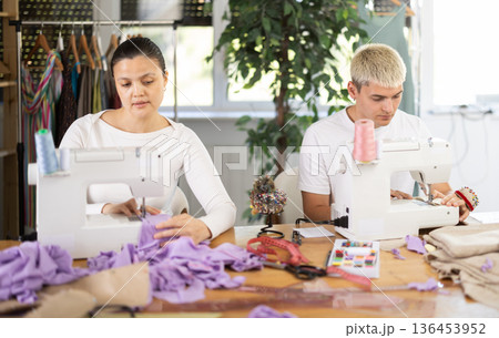 Two seamstresses male and female working on sewing machines in sewing workshop Two seamstresses male and female working on sewing machines in sewing workshop 136453952