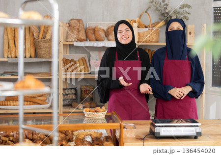 Two Muslim saleswomen stand in bakery shop, ready to greet customers 136454020