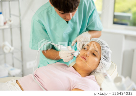 Young male cosmetologist doing ultrasound procedure to young woman Young male cosmetologist doing ultrasound procedure to young woman 136454032