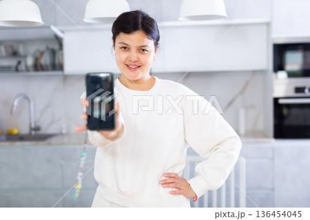 Young woman showing smartphone with blank screen in office kitchen 136454045