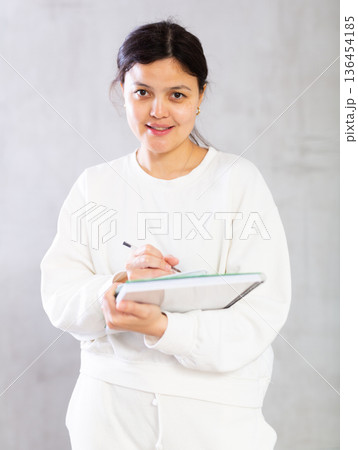 Smiling young female tutor or college student writing in workbooks Smiling young female tutor or college student writing in workbooks 136454185
