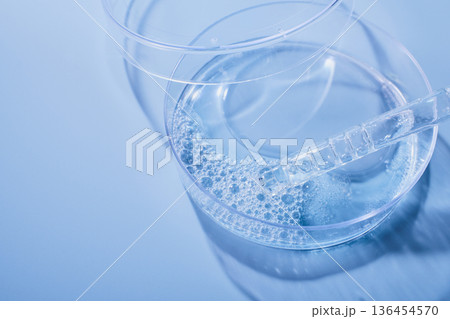 Petri dish holding blue liquid and pipette creating bubbles for cosmetic research 136454570