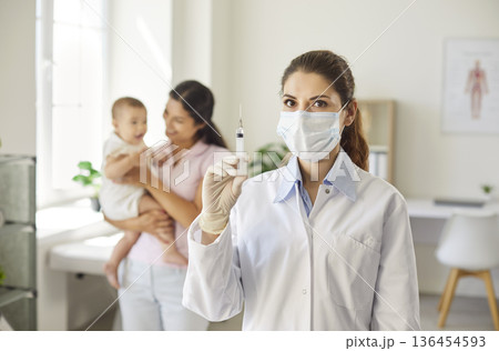 Confident nurse shows syringe mother with baby stands in modern pediatric clinic Confident nurse shows syringe mother with baby stands in modern pediatric clinic 136454593