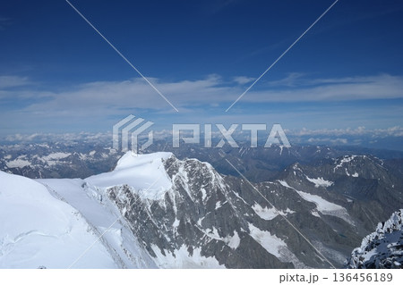 A stunning rock formation covered in snow, set against a clear blue sky with fluffy clouds in the background, creating a peaceful and breathtaking mountain landscape. A stunning rock formation covered in snow, set against a clear blue sky with fluffy clouds in the background, creating a peaceful and breathtaking mountain landscape. 136456189