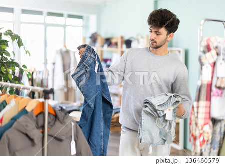Male shopper chooses fashionable jeans in clothing store Male shopper chooses fashionable jeans in clothing store 136460579