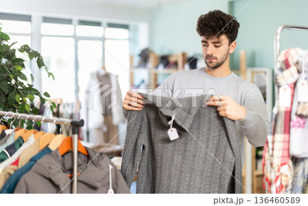 Guy choosing casual knit sweater in clothing outlet 136460589