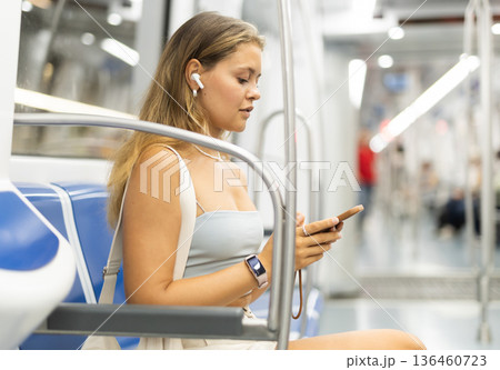 Woman standing in subway car with phone and headphones Woman standing in subway car with phone and headphones 136460723