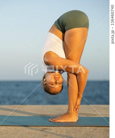Sportive girl practicing forward bend pose of yoga on seashore 136460740