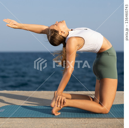 Athletic girl training camel position on mat on seashore 136460743