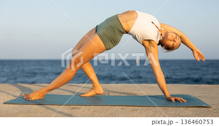 On windy day young slender woman does yoga near sea doing Chamatkarasana On windy day young slender woman does yoga near sea doing Chamatkarasana 136460753