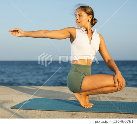 Sportive girl practicing seated yoga asana on seashore Sportive girl practicing seated yoga asana on seashore 136460761