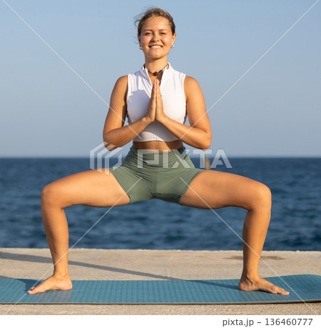 Young girl in sportwear doing stretching exercises for strong arms and abs and difficult yoga asana on the seashore on sunny day Young girl in sportwear doing stretching exercises for strong arms and abs and difficult yoga asana on the seashore on sunny day 136460777