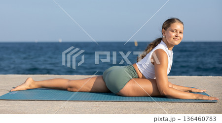 Sportive girl practicing pigeon pose of yoga on seashore 136460783