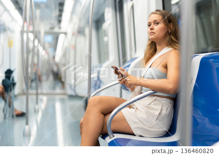 Young woman is sitting in subway car with phone, getting to work, school. 136460820