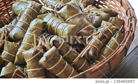 Sticky rice with coconut and banana filling, wrapped in banana leaves, cooked and placed in a basket. 136460897