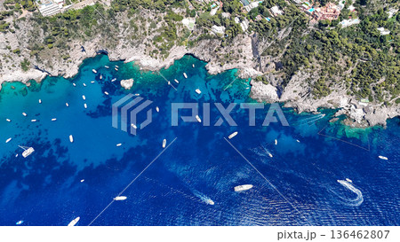 Vibrant turquoise waters surround rugged cliffs adorned with boats under the summer sun, showcasing nature's stunning beauty Vibrant turquoise waters surround rugged cliffs adorned with boats under the summer sun, showcasing nature's stunning beauty 136462807