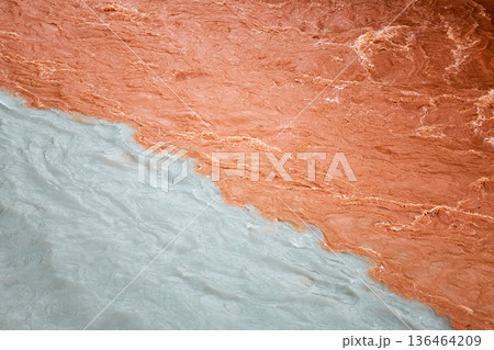 Confluence of two rivers with distinct colors. Brown muddy water meeting light blue glacier water. Natural phenomena background. Confluence of two rivers with distinct colors. Brown muddy water meeting light blue glacier water. Natural phenomena background. 136464209