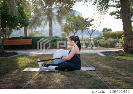 Pregnant Woman Doing Outdoor Stretching With Resistance Band And Exercise Ball On Mat Pregnant Woman Doing Outdoor Stretching With Resistance Band And Exercise Ball On Mat 136465446