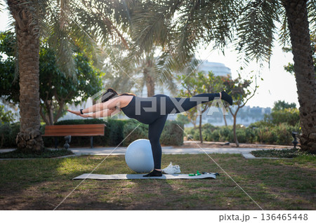 Woman Doing Balance Exercise With Stability Ball In Park For Outdoor Fitness And Flexibility 136465448