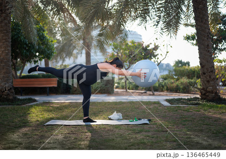 Woman Doing Balance Exercise With Stability Ball In Park For Outdoor Fitness And Flexibility 136465449