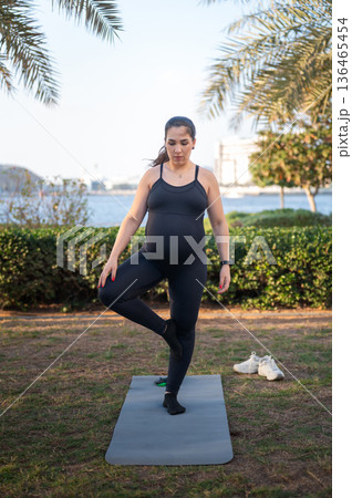 Pregnant Woman Doing Yoga Outdoors On Mat By Water For Fitness And Wellness 136465454
