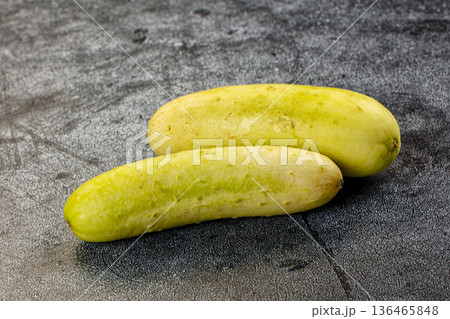 Two whole ripe white cucumbers on a dark textured stone background. 136465848