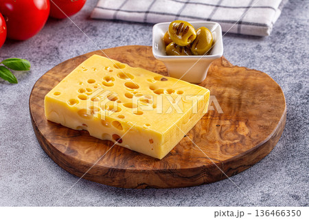 Block of Swiss cheese on a wooden cutting board with grilled olives and fresh tomatoes 136466350