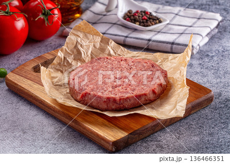 Raw hamburger patty on parchment paper ready for cooking, with fresh tomatoes and basil Raw hamburger patty on parchment paper ready for cooking, with fresh tomatoes and basil 136466351