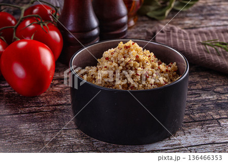 Healthy cooked tri-color quinoa in a bowl with fresh tomatoes and rosemary on a rustic wooden table 136466353