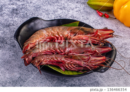 Fresh raw giant red prawns on a plate with chili peppers and tropical vegetables. Fresh raw giant red prawns on a plate with chili peppers and tropical vegetables. 136466354